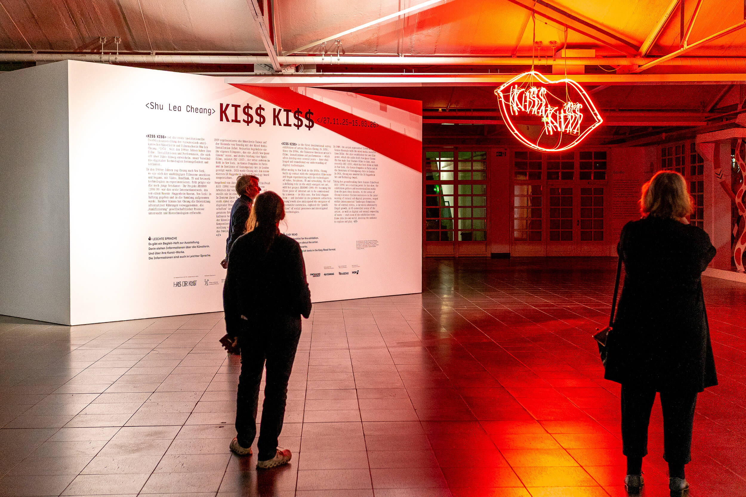 Büro Gestalten: Ausstellungstypografie »Shu Lea Cheang. KI$$ KI$$« (Ludwig Forum Aachen 2025/26), Wandtext (Foto quer, mit Besucher*innen)